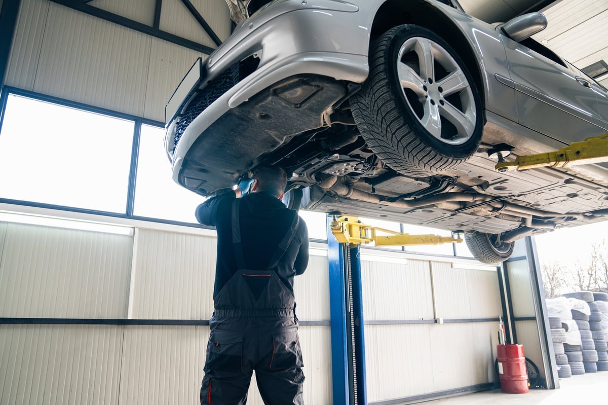 Modern servis atölyesinde kaldırılmış araç üzerinde çalışan teknisyen